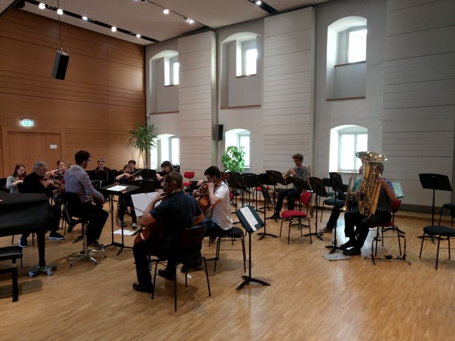 Orchester probt in einem Probenraum mit holzgetäfeltem Fußboden