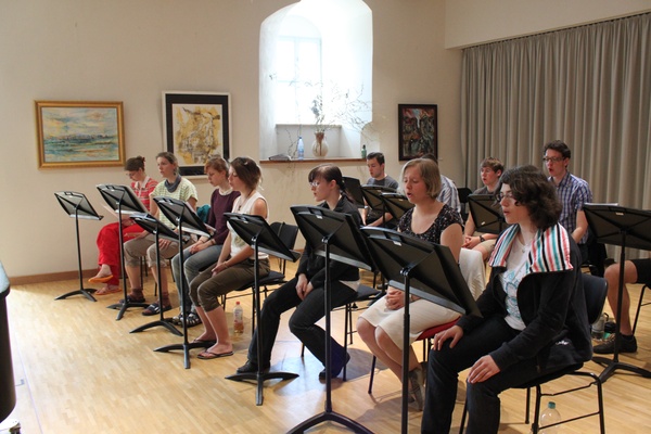 Sitzende Frauen und Männer bei einer Chorprobe mit Notenständern in einem Probenraum
